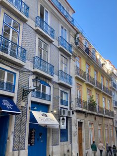 people are walking down the street in front of some buildings with balconies on them