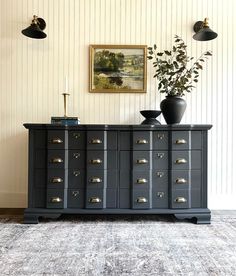 a black cabinet with two vases on top of it next to a painting and lamp