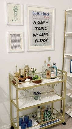 a bar cart with drinks on it in front of some pictures and other items hanging on the wall