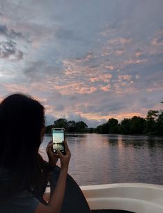 a woman sitting in a boat looking at her cell phone while the sun is setting