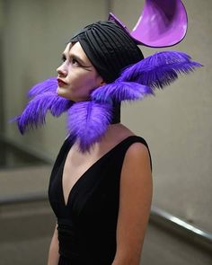 a woman with purple feathers on her head wearing a black dress and a large hat