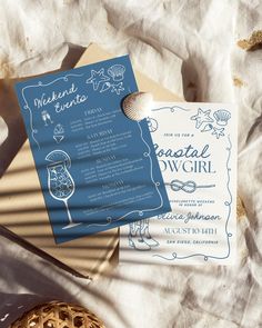 two wedding cards sitting on top of a bed next to a basket with seashells