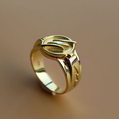 a gold ring with an oval design on the front and side, sitting on a brown surface