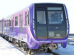 a purple train traveling down tracks next to snow covered ground