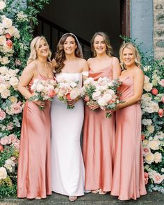 four bridesmaids pose for a photo in front of a floral arch with their bouquets