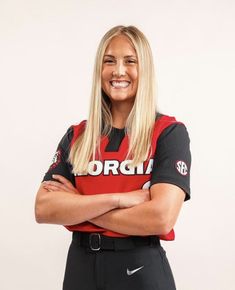 a woman with her arms crossed posing for a photo wearing a baseball uniform and smiling at the camera