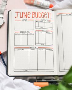 an open planner book sitting on top of a bed next to a watch and pen