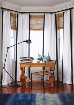 a desk with a lamp and some books on it in front of a large window