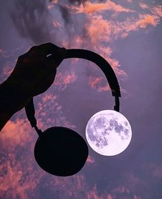 the moon is seen in the night sky with silhouettes of hands holding an object