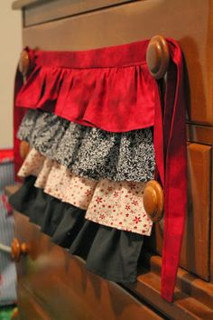 a red and black skirt hanging on the side of a wooden dresser next to a christmas tree