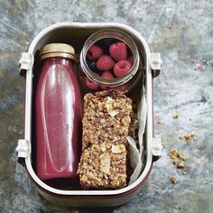 a lunch box with granola, raspberries and juice