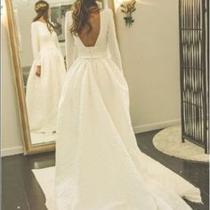 a woman is standing in front of a mirror wearing a wedding dress with long sleeves