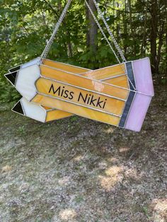 a stained glass sign hanging from the side of a tree in front of some trees