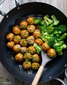 meatballs and broccoli are being cooked in a skillet with a wooden spoon