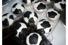 cupcakes decorated with black and white frosting in a plastic container on a counter