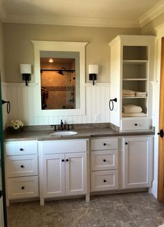 a bathroom with white cabinets and gray counter tops, along with an open door leading to another room