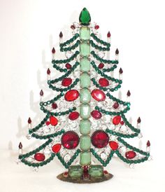 a small christmas tree made out of glass beads and jewels on a white surface with a green base