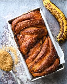 a loaf of bread in a box next to a banana and cinnamon sprinkled sugar