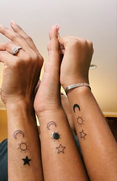 three people with tattoos on their arms holding hands up to the sky and stars above them