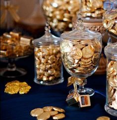 many glass jars filled with gold coins on a blue table cloth and some are sitting next to each other