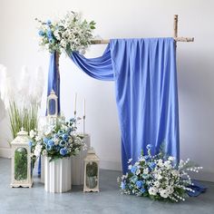 blue and white flowers are on display in front of an arch decorated with draping