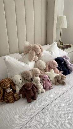 stuffed animals are lined up on the edge of a bed with white sheets and pillows