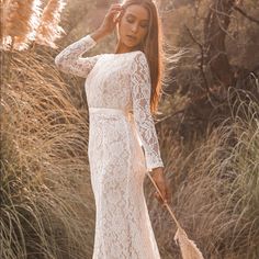 a woman in a white lace dress holding a broom and posing for the camera with her hands behind her head