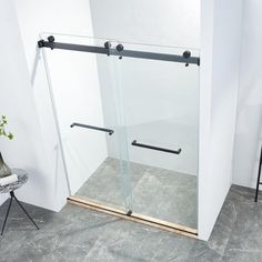 a bathroom with a glass shower door next to a white chair and potted plant