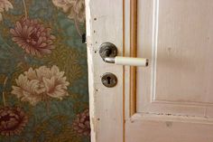 an open door with a white handle on it and floral wallpaper behind the door