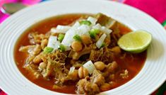 a white plate topped with meat and beans covered in sauce next to a lime slice