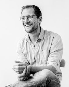 a black and white photo of a smiling man with his hands folded in front of him