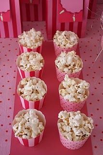 some pink paper cups filled with popcorn on top of a red and white table cloth