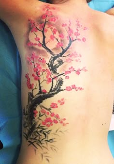 a woman's back with a tree and birds tattoo on her left side ribcage