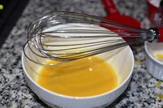 a white bowl filled with yellow liquid and whisk on top of a counter