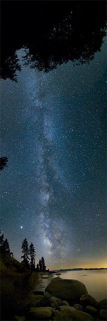 the night sky is filled with stars and clouds above some rocks in front of a body of water