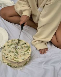 a woman sitting on a bed with a cake and knife in front of her face