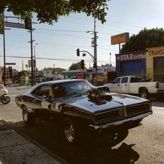 an old muscle car is parked on the side of the road in front of a gas station