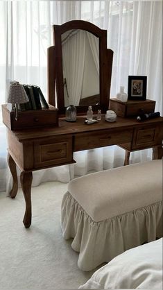 a dressing table with a mirror and stool in front of a white curtained window