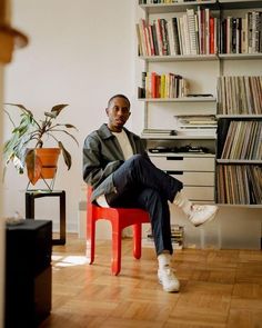 a man sitting on a red chair in front of a bookshelf