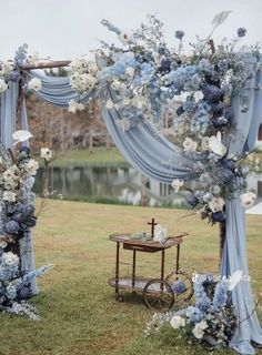 an outdoor wedding setup with blue and white flowers on the arch, decorated with sheer draping