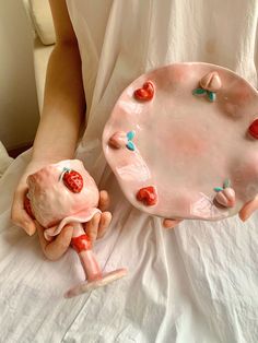 a person holding a pink plate with strawberries on it next to a small doll