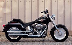 a black and silver motorcycle parked in front of a wooden building with a metal fence behind it