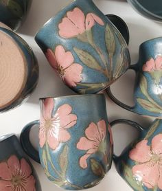 four tea cups with pink flowers painted on them are sitting next to each other in the middle of a table