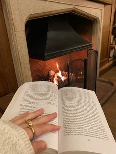 a person reading a book in front of a fire place with their hands resting on an open book