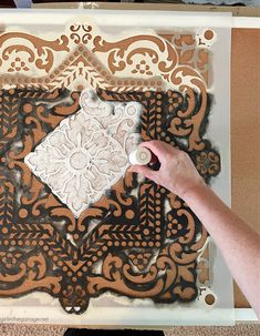 a person is painting an ornate design on a piece of cardboard with white paint and brown paper