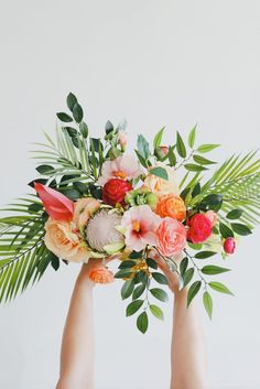 two hands holding flowers and greenery against a white background