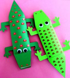 two green paper lizards with eyes and legs on a pink surface next to each other