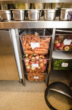 an assortment of fruits and vegetables in bins under a stainless steel counter top,