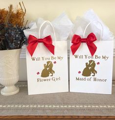 two paper bags with red bows are sitting on a table next to a white vase