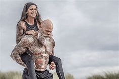 a woman carrying a man on her back in the air with sand and grass behind her